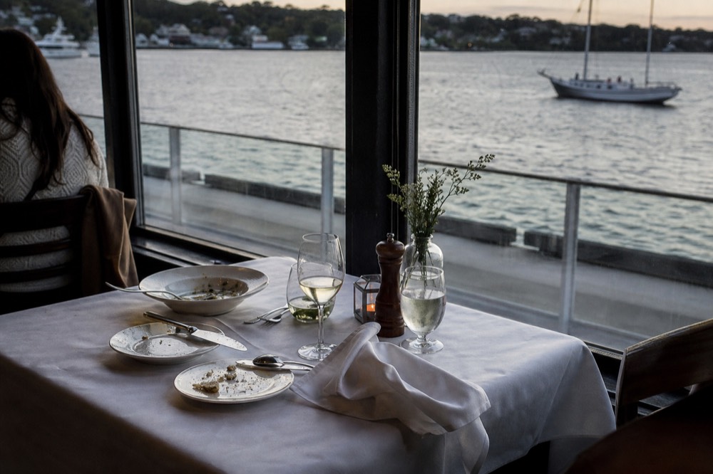 A plated dinner table set beside a harbor window on a cruise ship