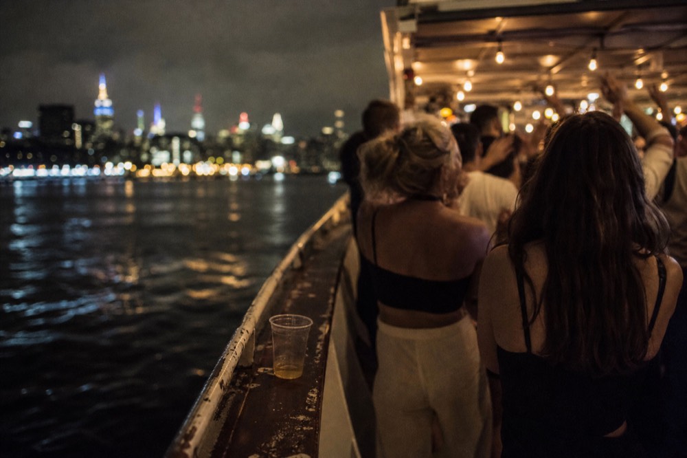 Guests dancing on an open cruise deck at night with city lights beyond