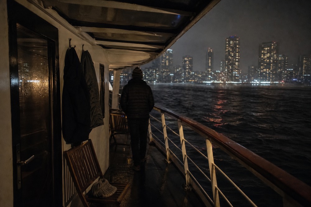 Guests wearing light jackets on a cruise deck with city lights beyond