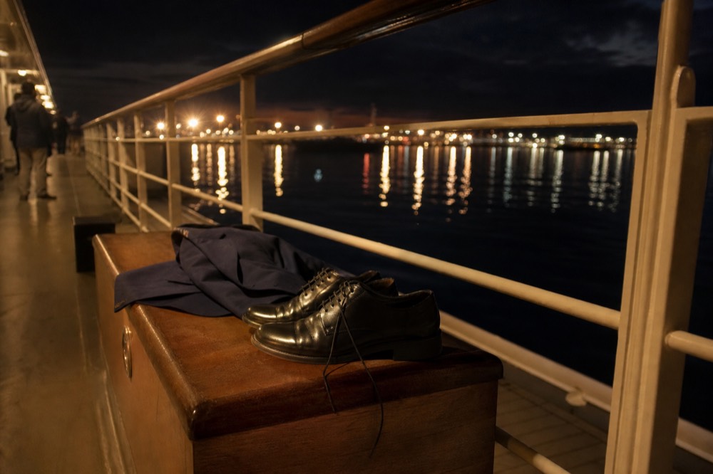 Dress shoes and a folded blazer beside a railing on an evening harbor cruise