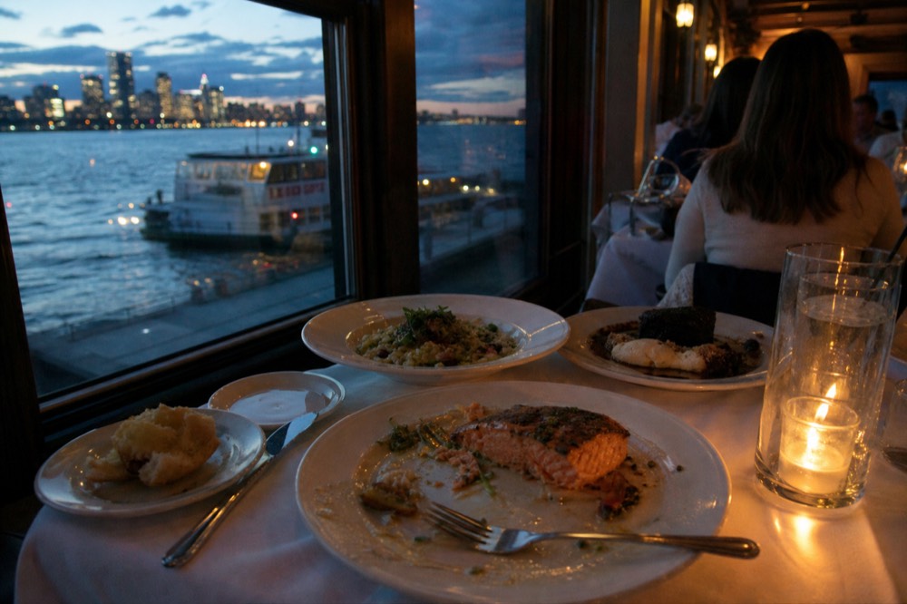 Plated three-course dinner set on a table beside a harbor window at dusk