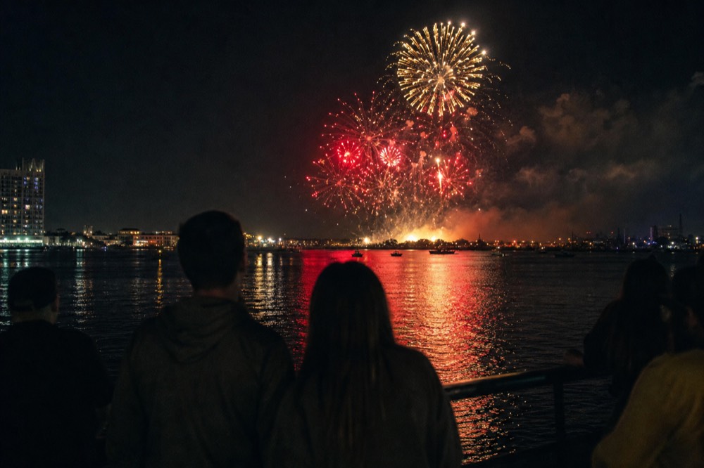 Fireworks bursting over Boston Inner Harbor with dark water and city lights below