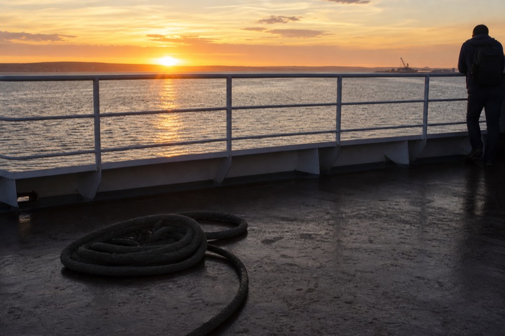 The sun setting over Boston Harbor behind a cruise vessel deck railing